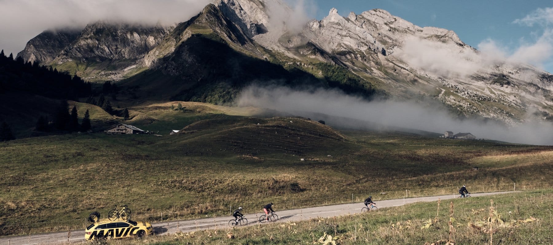 Low cloud descends over cyclists during the Route Des Grandes Alpes, creating atmospheric conditions